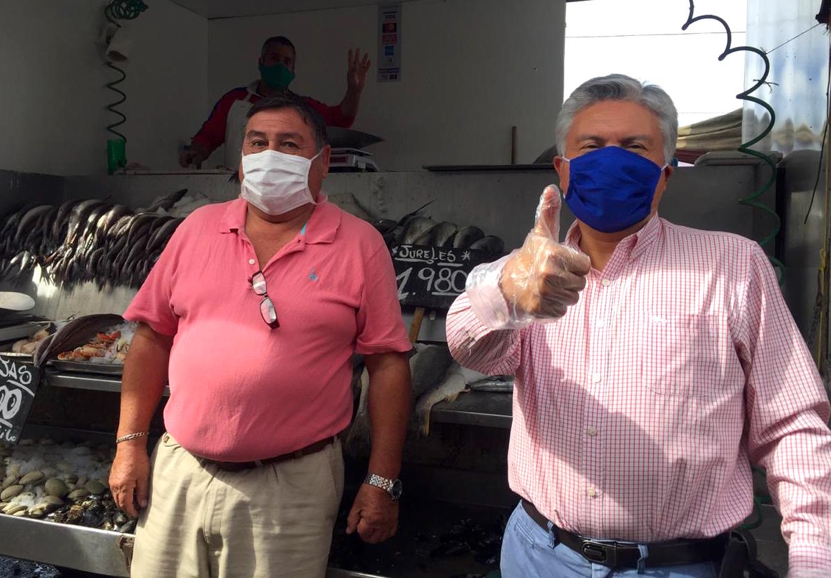 Two men standing at fish market. Both wear face masks.