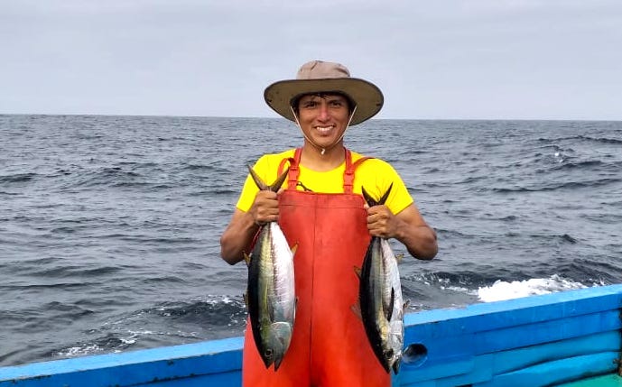 Peruvian fisher standing in a boat, holding two fish