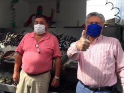 Two men standing at fish market. Both wear face masks.