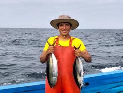 Peruvian fisher standing in a boat, holding two fish